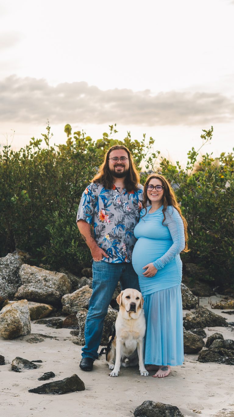 Maternity portrait of a couple with their dog on the rocks by the water