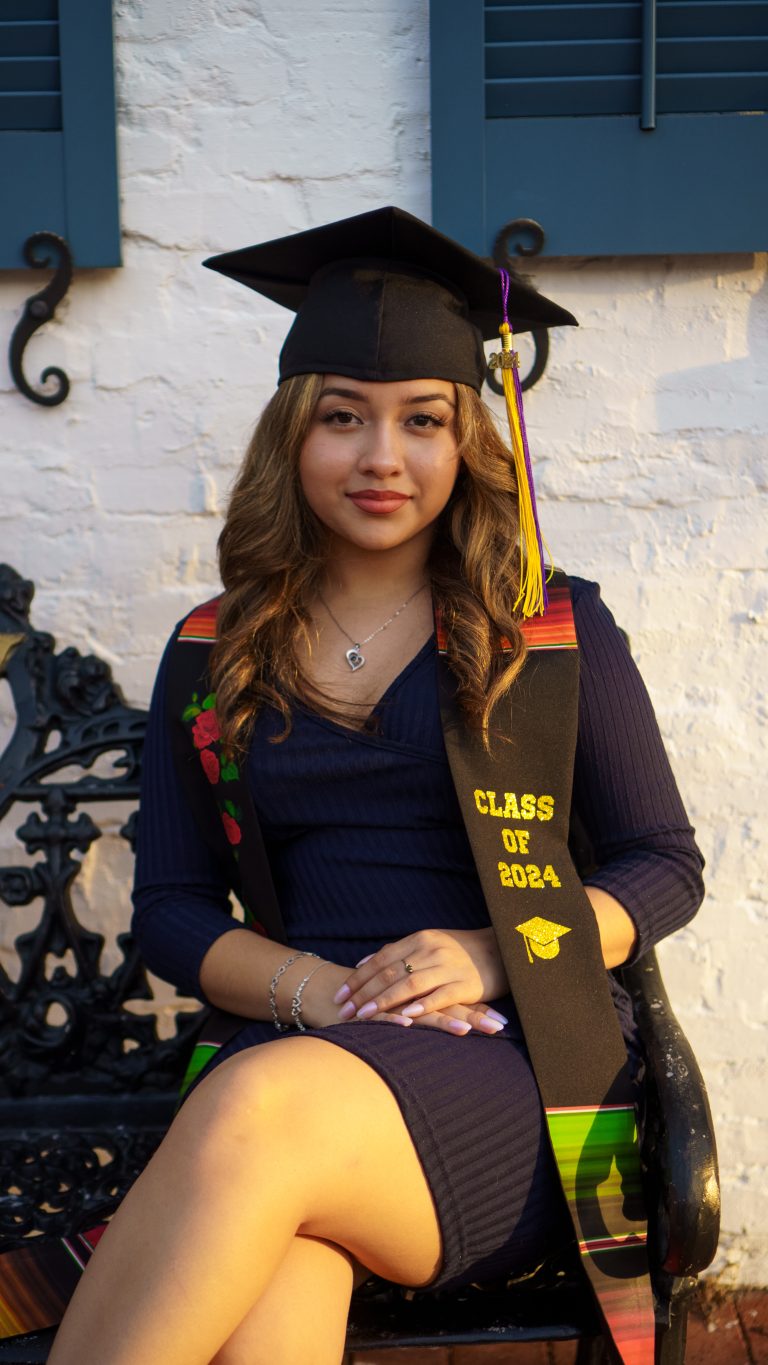 Senior graduation portrait in cap and stole by a white brick wall