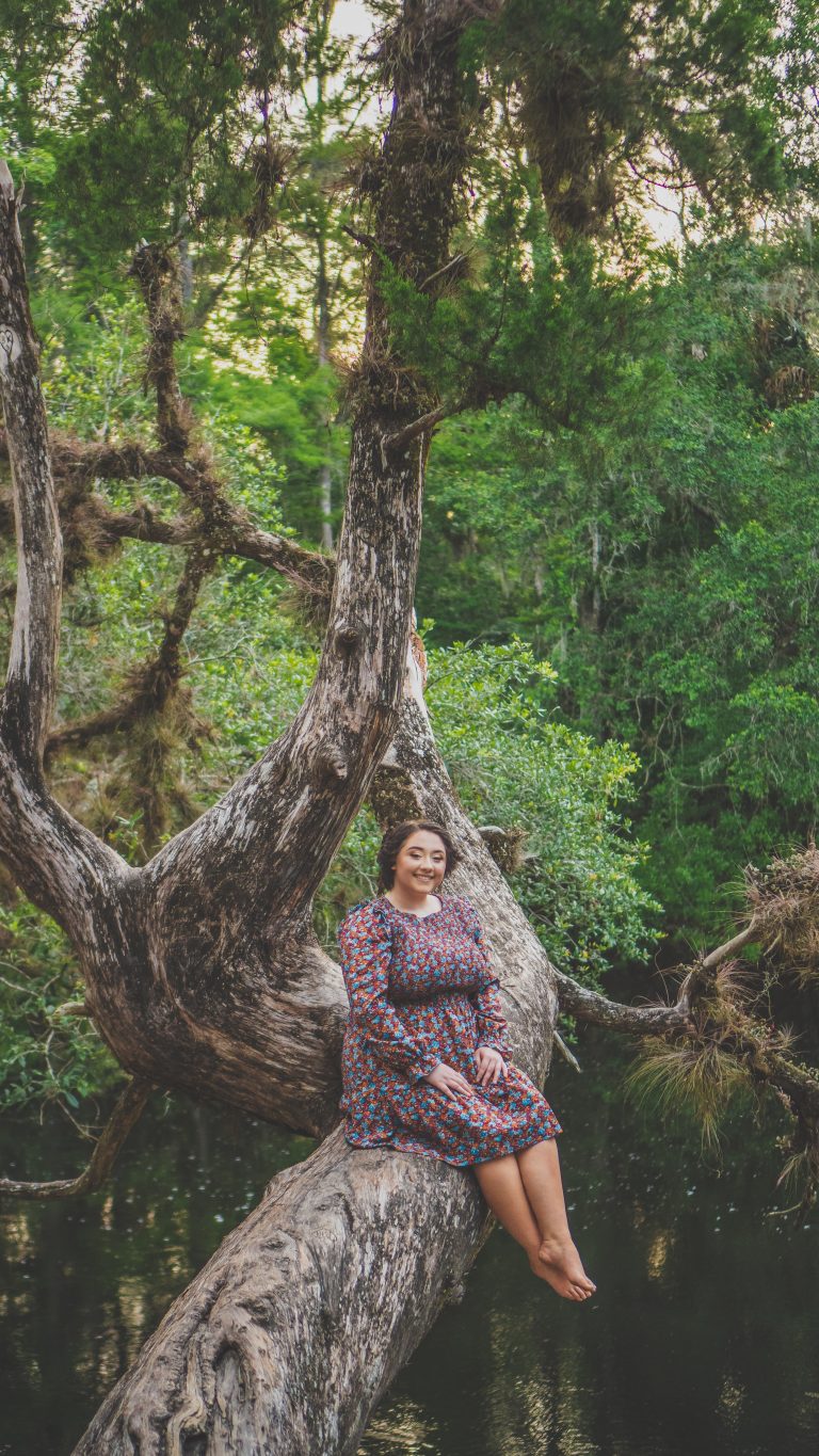 Portrait of a young woman in a floral dress sitting in a large oak tree