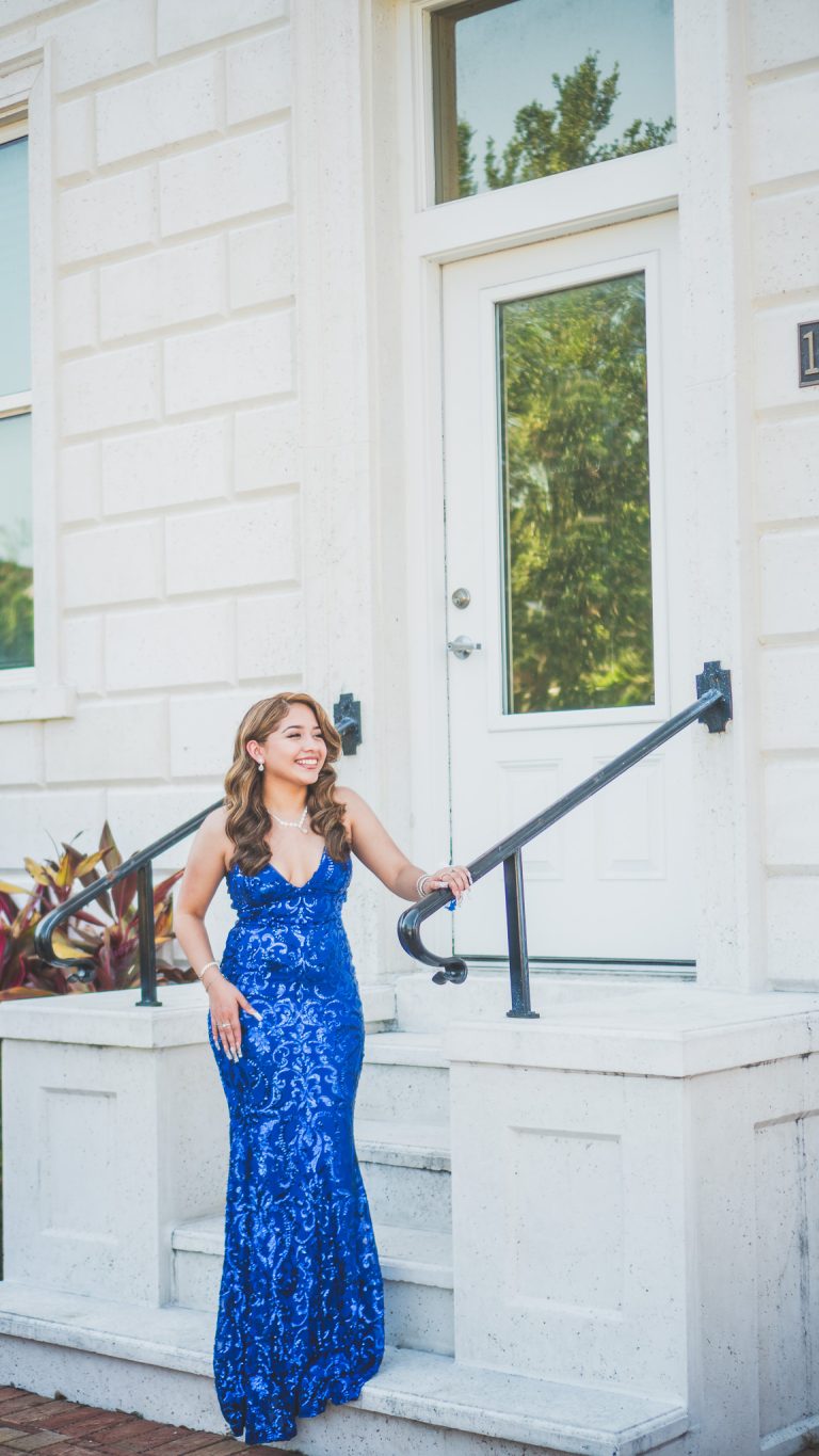 Senior portrait of a young woman in a royal blue sequin gown on white steps